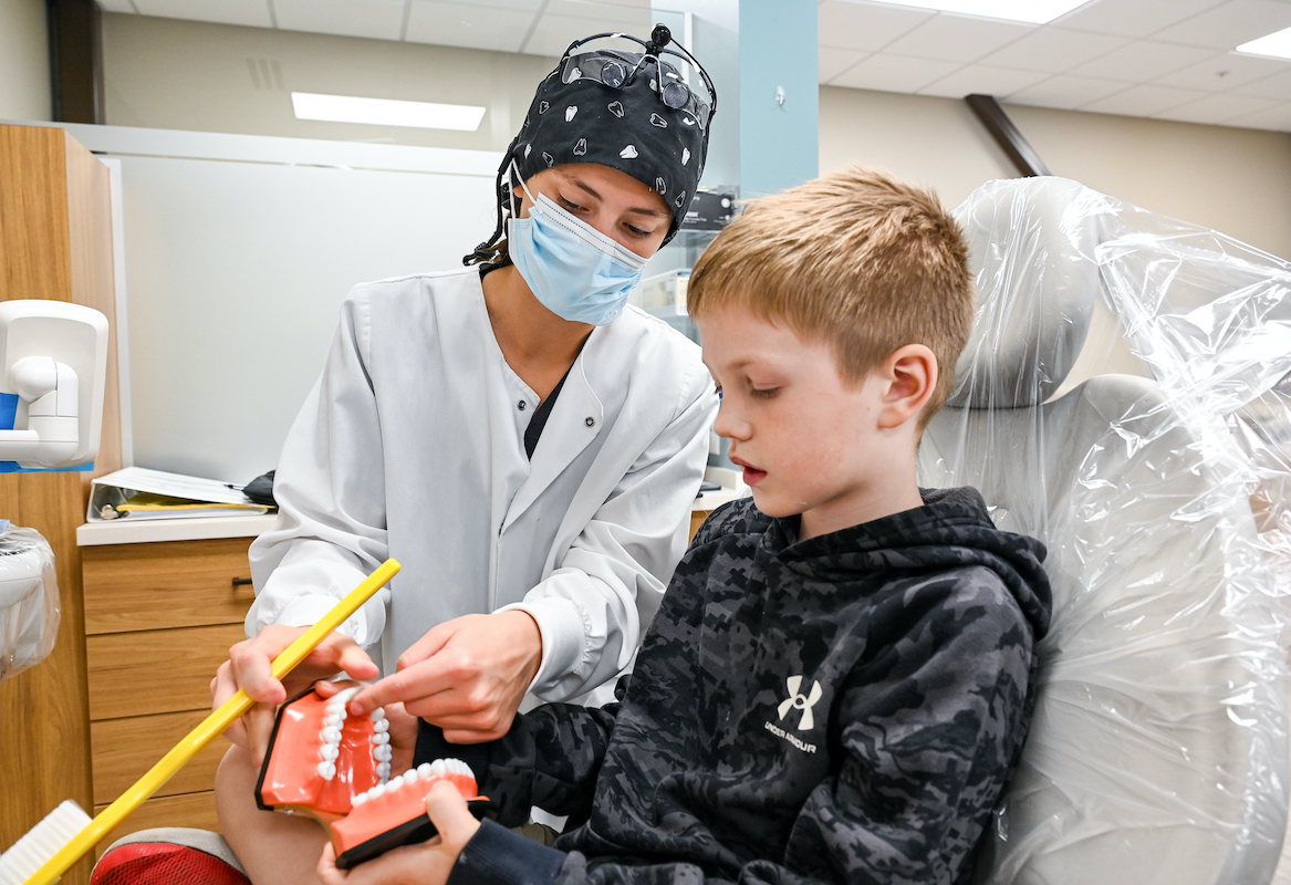 student explaining to young patient using dental model